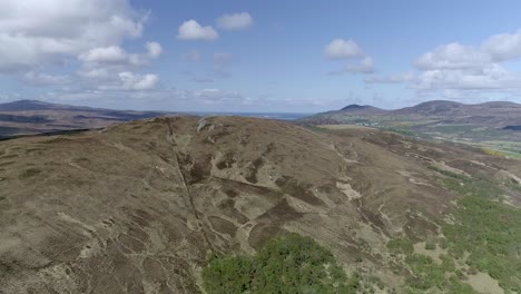 Aerial-tracking-past-a-heathland-hill-to-reveal-a-small-lake-and-a-road-surrounded-by-flowering-yellow-gorse-bushes