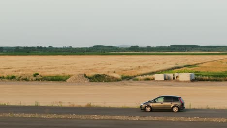 Grey-car-driving-on-an-unfinished-tarmac-road,-aerial-close-up-tracking-shot