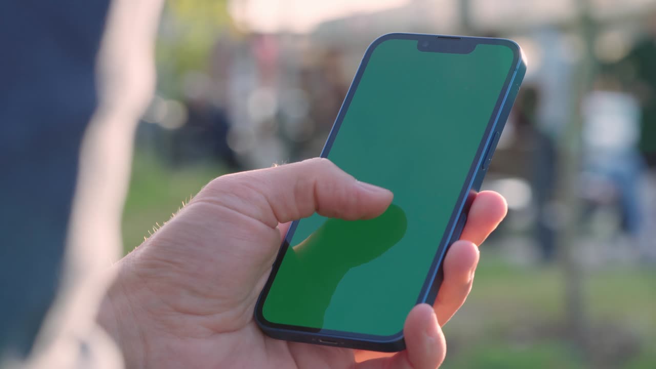 primer plano de 4k de la mano del hombre sosteniendo un teléfono inteligente con pantalla de maqueta verde llave croma al aire libre