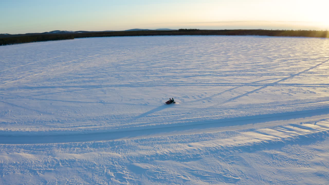 vista aérea de un solo conductor de motos de nieve que viaja rápido a través de un vasto y nevado desierto de invierno nórdico lejos del amanecer