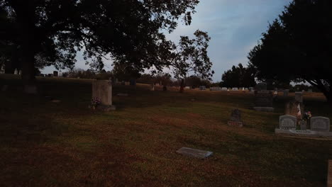 flying low over peaceful green field in cemetery, green trees all around