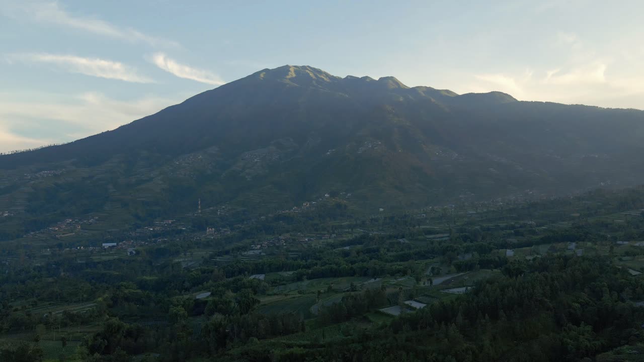 Terbang di atas pemandangan pedesaan Indonesia dengan Gunung Merbabu di latar belakang pada pagi hari