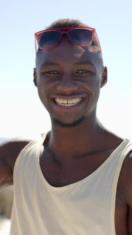 vertical video: smiling african american man wearing sunglasses enjoying sunny day at beach