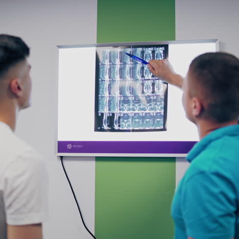 back view of a male doctor and patient examining x-ray in the hospital. specialist shows the problem areas of the back on the x-ray photograph to a young man.
