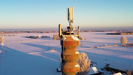 Water-tower-with-mobile-network-antennas-in-cold-winter-morning,-aerial-pedestal-up