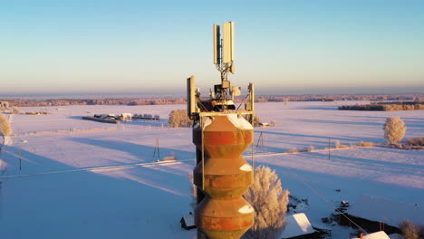 Torre-De-Agua-Con-Antenas-De-Red-Móvil-En-La-Fría-Mañana-De-Invierno,-Pedestal-Aéreo-Arriba