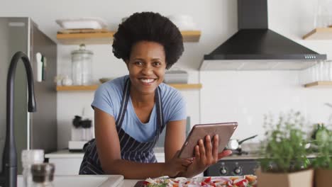 portrait of happy african american woman preparing dinner using tablet in kitchen