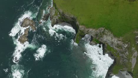 aerial birdseyeview of waves crashing on a coastal cliff with bright green grass on the island of achill in ireland