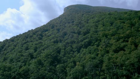 A-tilt-reveal-of-the-former-spot-of-the-Old-Man-in-The-Mountain-rock-formation-atop-a-lake-and-green-trees