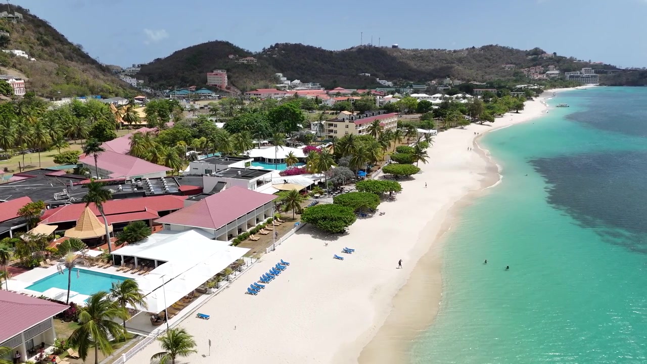Drone che vola sopra Grand Anse Beach, mostrando proprietà di resort costieri di lusso, litorale di sabbia bianca e acque oceaniche turchesi incontaminate a Grenada, Caraibi