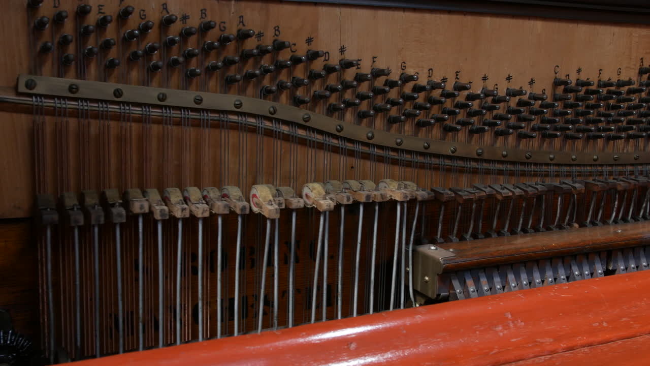 A piano with exposed internal strings and hammers is displaying musical note labels above the tuning pins revealing detailed mechanical components of the instrument