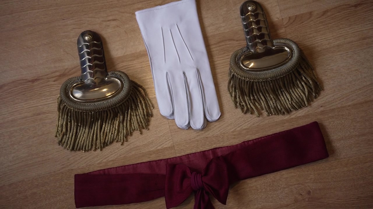 Eleganti accessori militari: spalline dorate, guanti bianchi e una fascia rossa, adagiati su legno