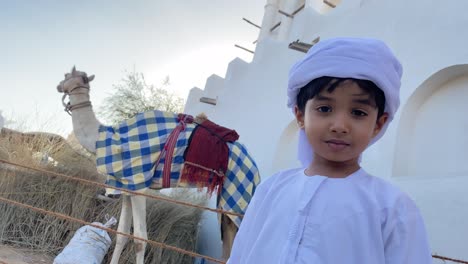 feliz niño emiratí sonriente y camello en el fondo tradicional