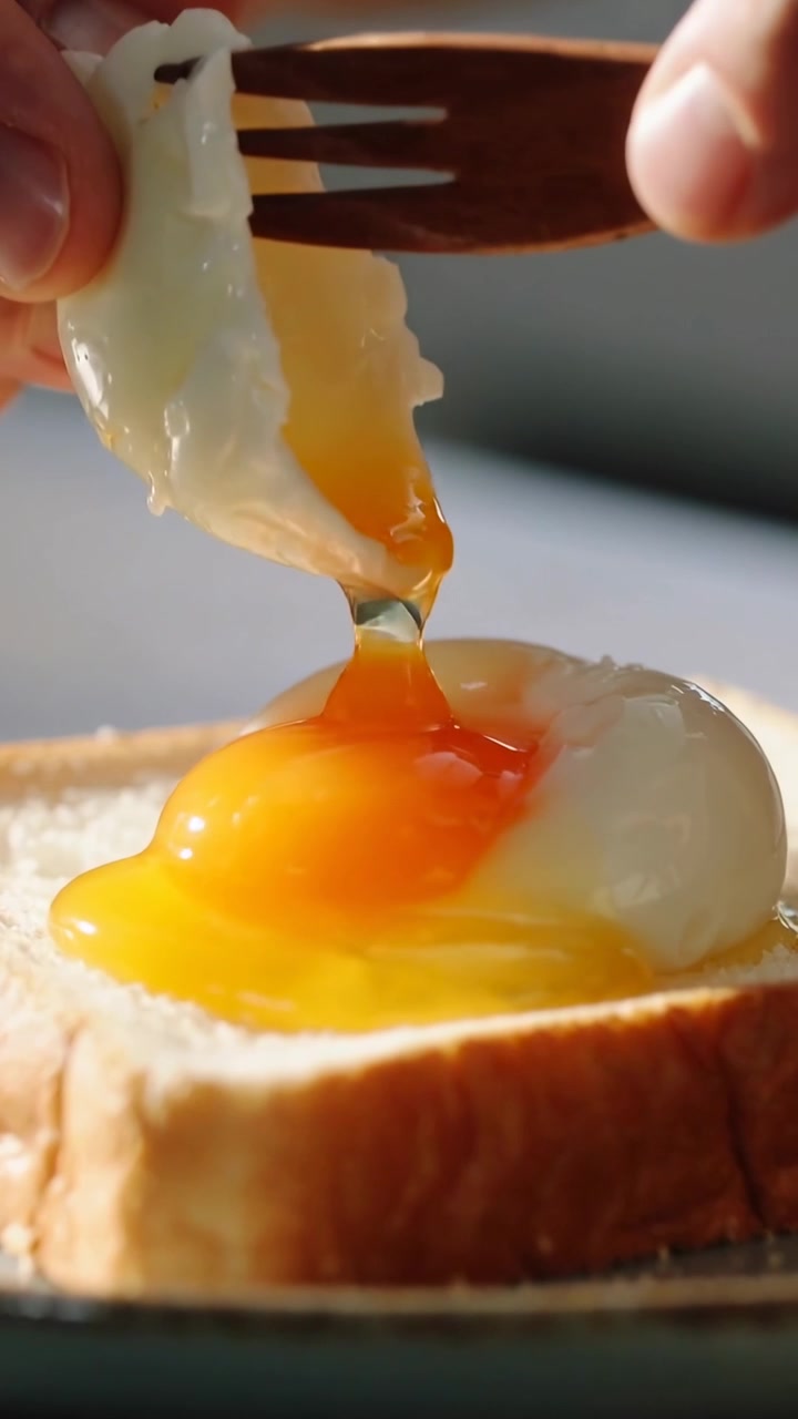 Vertical video: Using fork wooden spoon hands pulling poached egg in kitchen yolk spilling on toast
