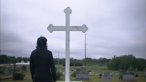 young, religious man in black suit worshipping and praying in front of christian cross