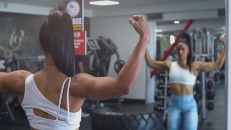 entrenadora de fitness femenina flexionando sus músculos y cuerpo frente a un espejo en el gimnasio