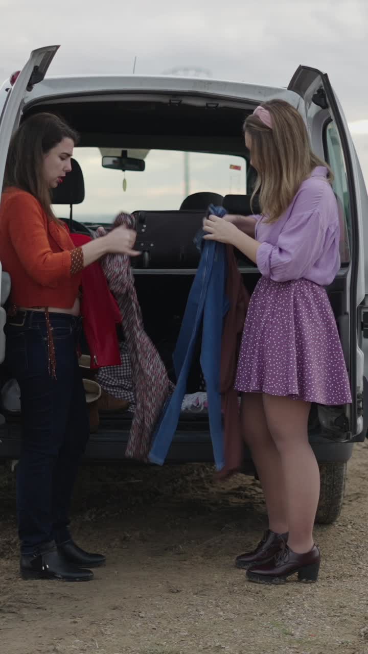 Two women unpacking clothes from a van