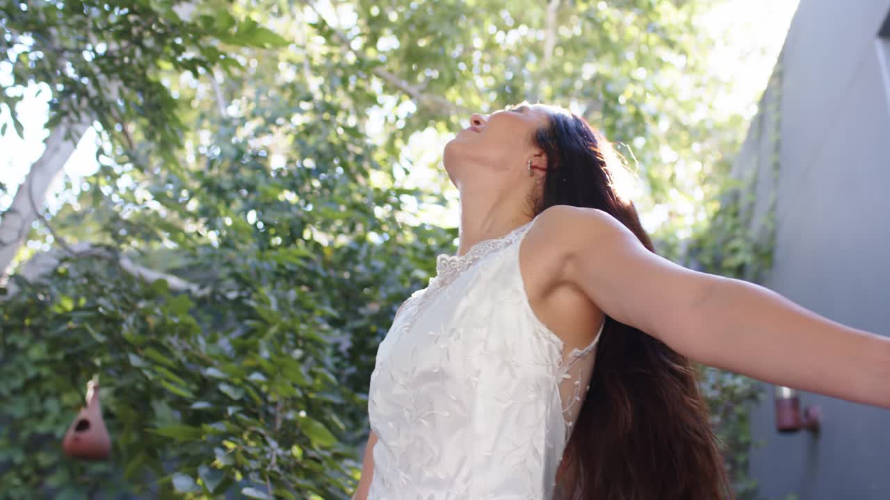 Luce screziata che avvolge una donna in abito di pizzo in giardino, mentre si inarca, si gira verso la fotocamera e abbassa la testa.