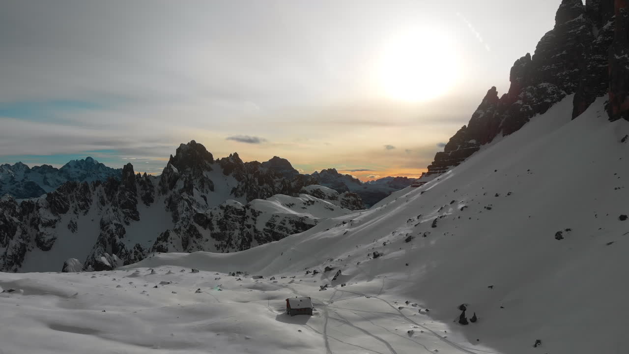 Vista aerea di una baita in legno isolata in un paesaggio montano innevato al tramonto