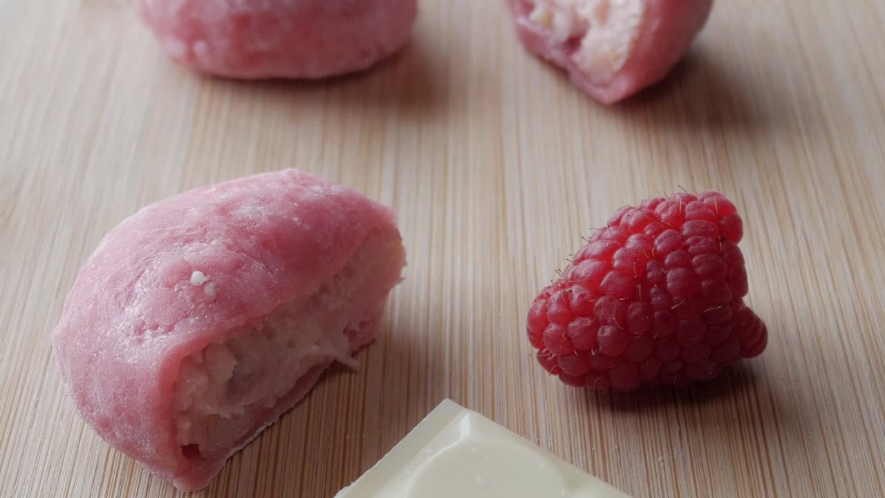 Soft pink strawberry mochi with white chocolate and raspberries on a wooden surface