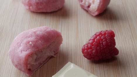 soft pink strawberry mochi with white chocolate and raspberries on a wooden surface