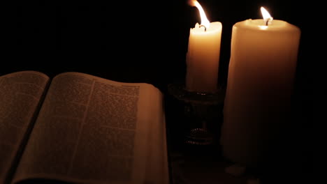 open holy bible lit by candle light in a hidden, dark place : pan left slow