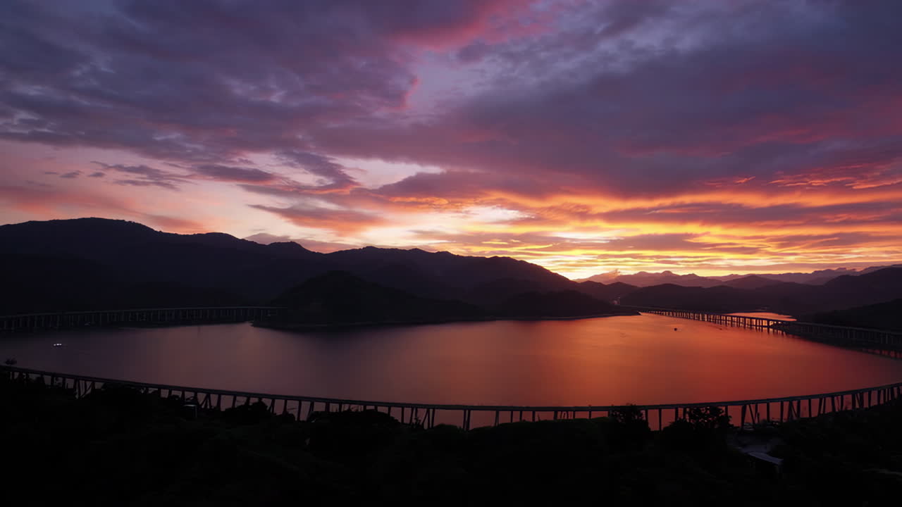 Dramatic Sunset Over a Lake with a Long Curving Bridge and Mountains