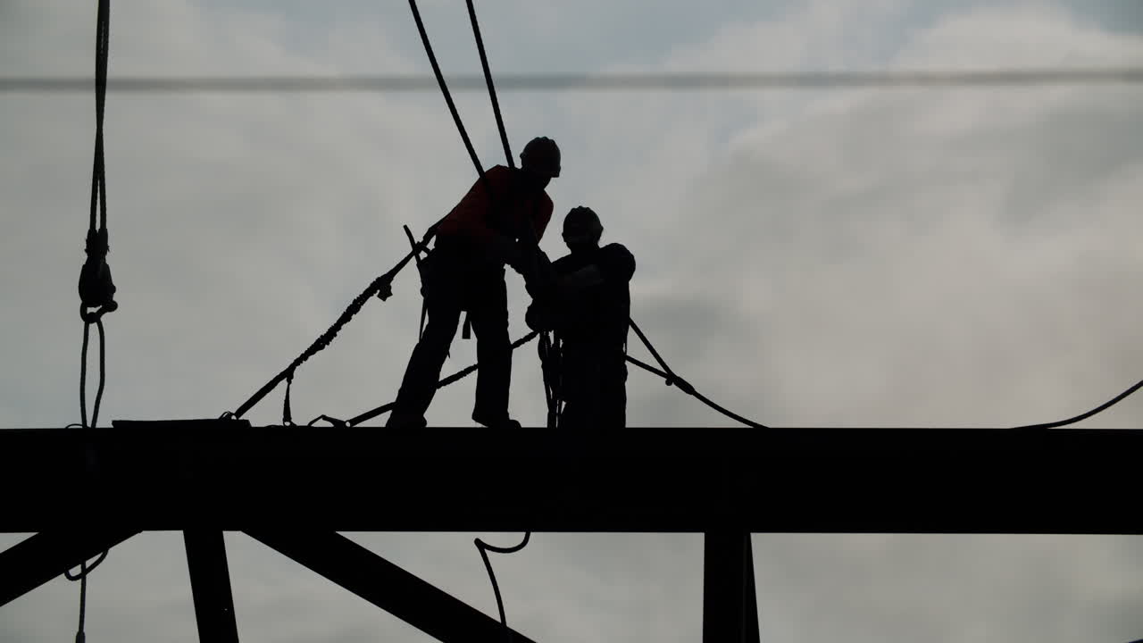 Silhouetted Construction Workers on a High Beam