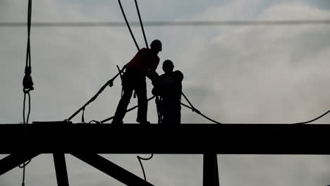 silhouetted construction workers on a high beam