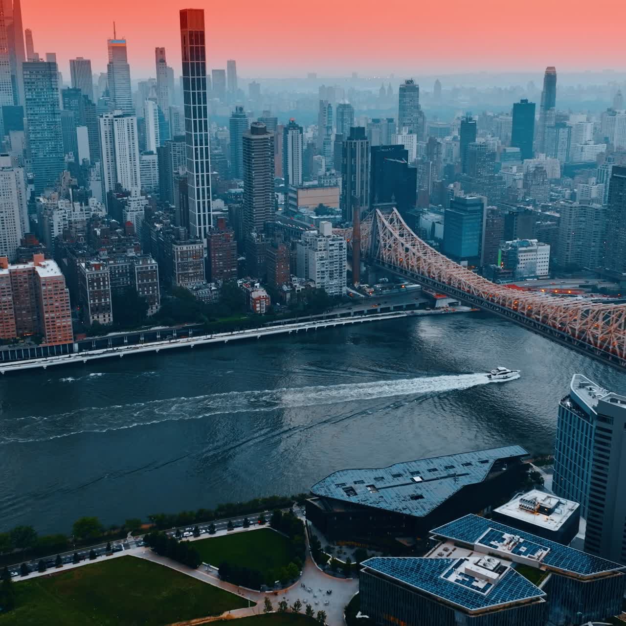 Yacht sailing by the river to go under Queensboro Bridge over East River. Splendid view on New York skyscrapers under pink sky at sunset. Aerial perspective