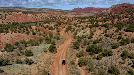 Aerial-shot-of-the-dusty-road-traveling-over-a-car-looking-at-the-landscape-of-Vermilion-Cliffs,-in-northern-Arizona-and-southern-Utah