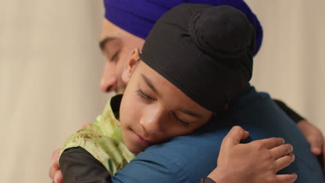 close up studio shot of sikh father embracing son both wearing turbans against plain background 2