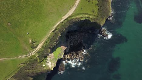 Olas-Chapoteando-En-Las-Rocas-Por-El-Paseo-Costero-De-Port-Isaac-Village-En-Inglaterra--Aéreo