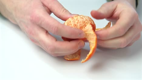 close up footage of man peeling an orange on white table