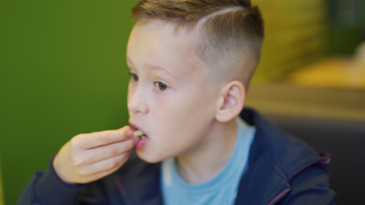 Young happy teenager eating fries and burger sitting in cafe in city. Boy in a fast food cafe. Harmful nutrition