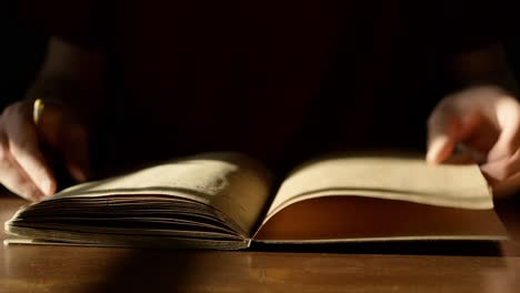 close up of hands flipping through organic beige sketchbook in harsh sunlight on brown table