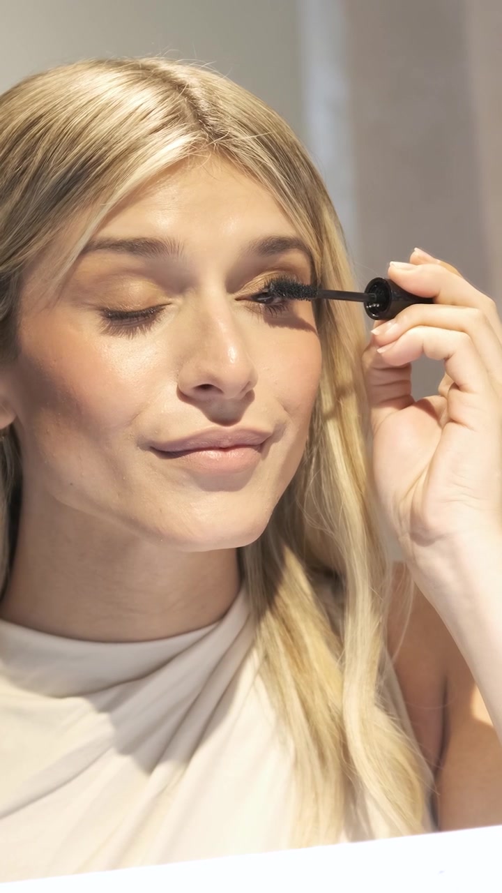 Young Woman Applying Mascara in Front of a Mirror