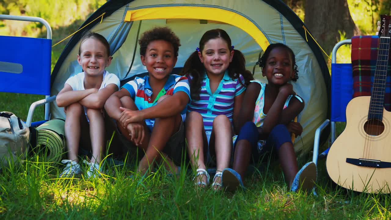 Kinder sitzen vor Zelt auf Campingplatz