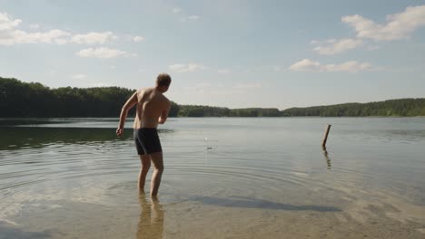 lone man half naked throwing stone at jezioro glebokie lake in poland