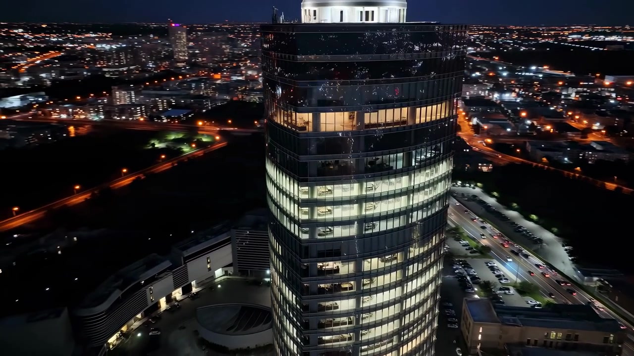 Vista aérea de um horizonte urbano sereno à noite, apresentando edifícios cilíndricos altos iluminados e uma rede de estradas, exibindo materiais de vidro e metal em um cenário de desenvolvimento urbano