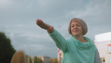 athlete performing hamstring stretches outdoors with arm extended forward wearing teal sportswear on cloudy day in urban park setting showcasing fitness strength flexibility and positive energy
