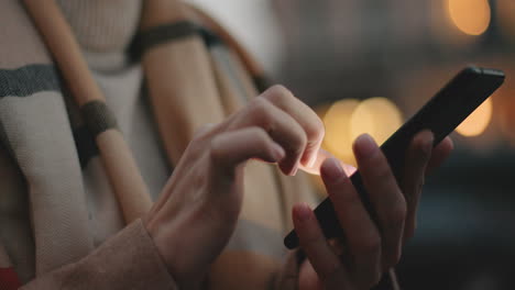 vista de primer plano de las manos de una mujer de negocios caucásica enviando mensajes de texto en su teléfono inteligente en la calle con luces de la ciudad en el fondo