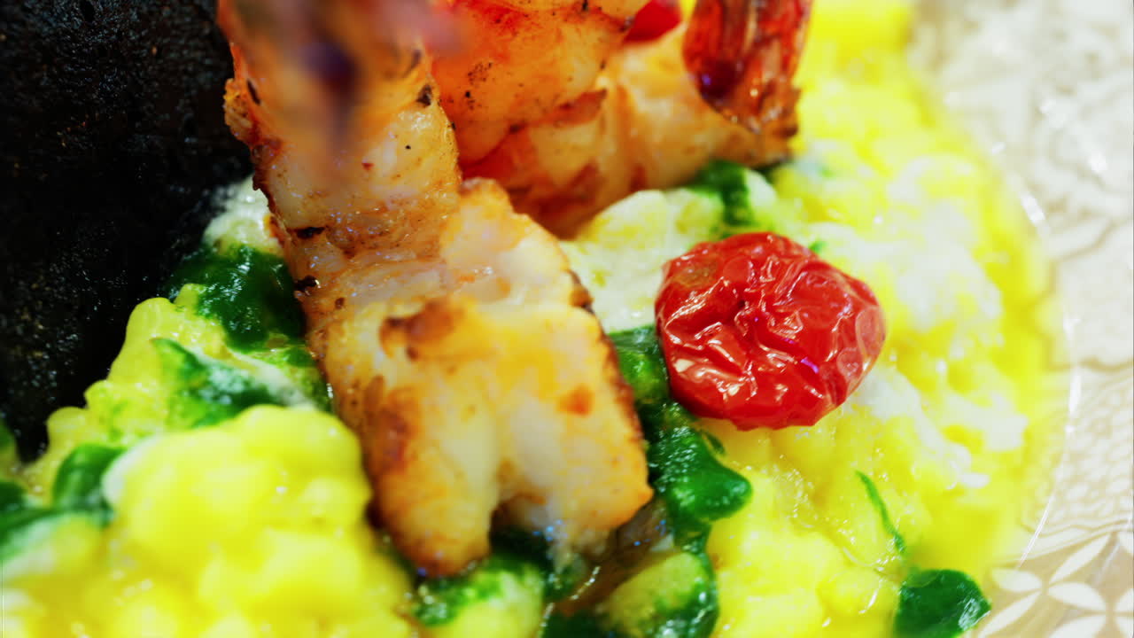 Close up of saffron risotto topped with grilled prawns and roasted cherry tomatoes