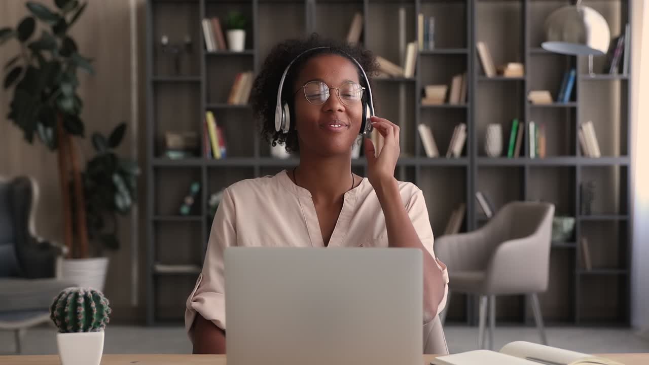 Woman wear headphones listen song seated at desk with laptop
