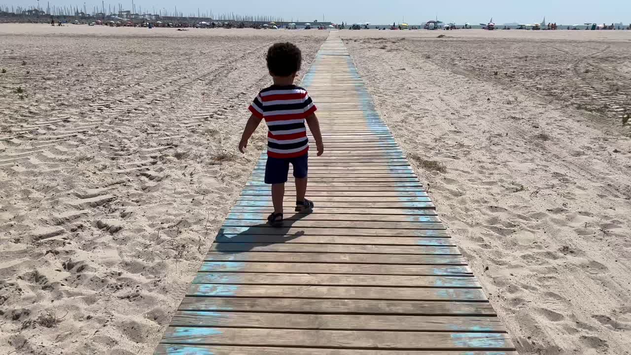 niño africano de dos años caminando sobre una puerta de madera en una playa de arena blanca en valencia, españa
