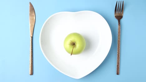 cutlery and empty plate with green apple on blue background