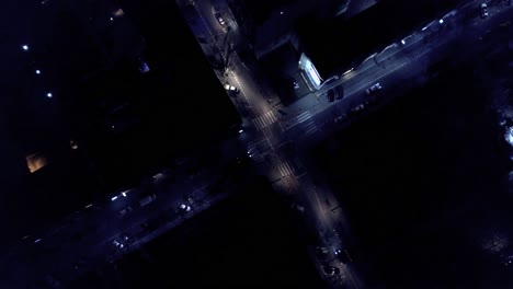 Vertical-top-down-aerial-view-of-traffic-on-street-intersection-at-night