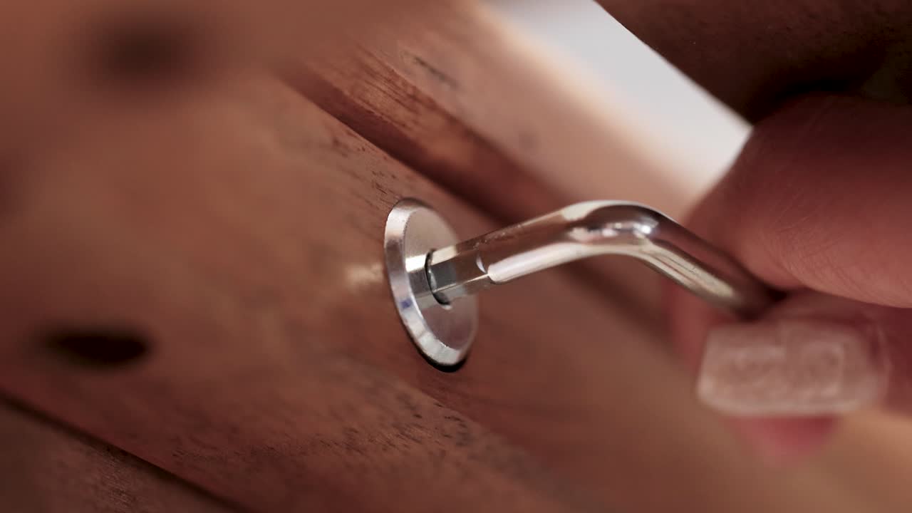 Close-up of a hand using a hex key to tighten a screw in wooden furniture, highlighting precision and craftsmanship