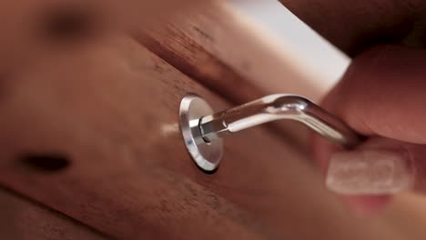 close-up of a hand using a hex key to tighten a screw in wooden furniture, highlighting precision and craftsmanship