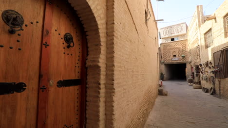 Traditional-wooden-door-on-a-quiet,-narrow-street-in-Sbeitla,-with-warm-tones-and-historical-architecture